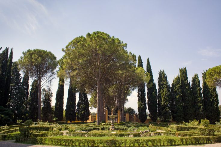 Un grand jardin avec des pins et des cyprès, entouré de parterres de fleurs bien entretenus.