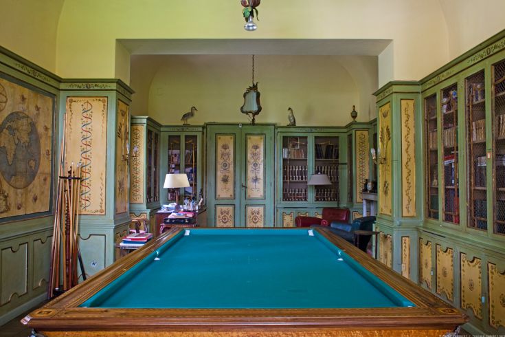 Une pièce confortable avec une table de billard et des meubles de style classique, agrémentée d'étagères remplies de livres.