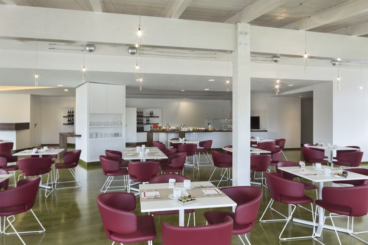 Ambiente accogliente e luminoso, con tavoli chiari e sedie rosse. Spazio adatto per pranzi e cene in compagnia.