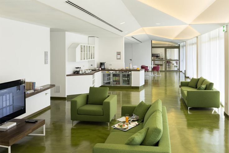 Ambiente contemporaneo con arredi verdi, cucina a vista e area relax, perfetto per momenti di convivialità.