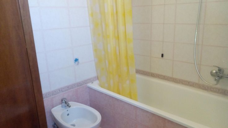 Bagno semplice con vasca e doccia, impreziosito da tende gialle per creare un'atmosfera luminosa.