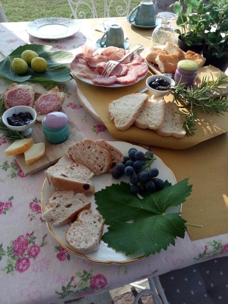 Un brunch all'aperto con salumi, formaggi e pane fresco, circondato dalla natura.