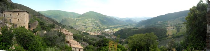 Scena di un borgo medievale disabitato, incastonato tra colline verdi e uliveti.