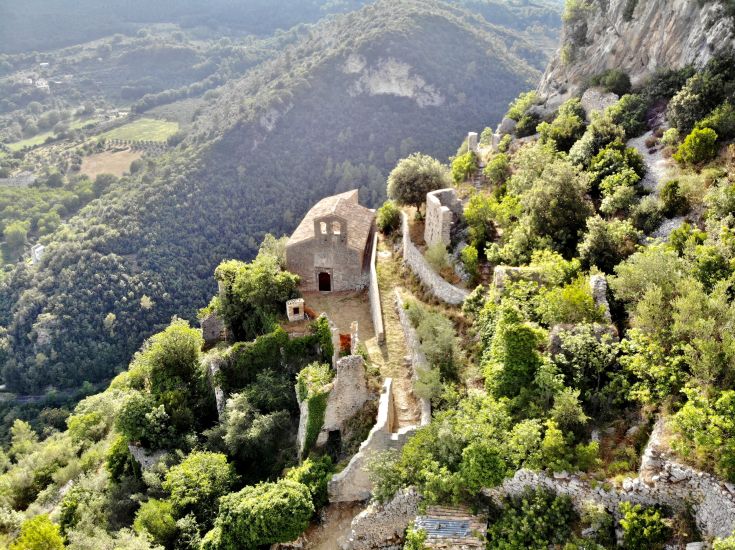 Un antico borgo in stato di abbandono, circondato da vegetazione e situato in un'area naturale con vecchi edifici e giardini a terrazza.