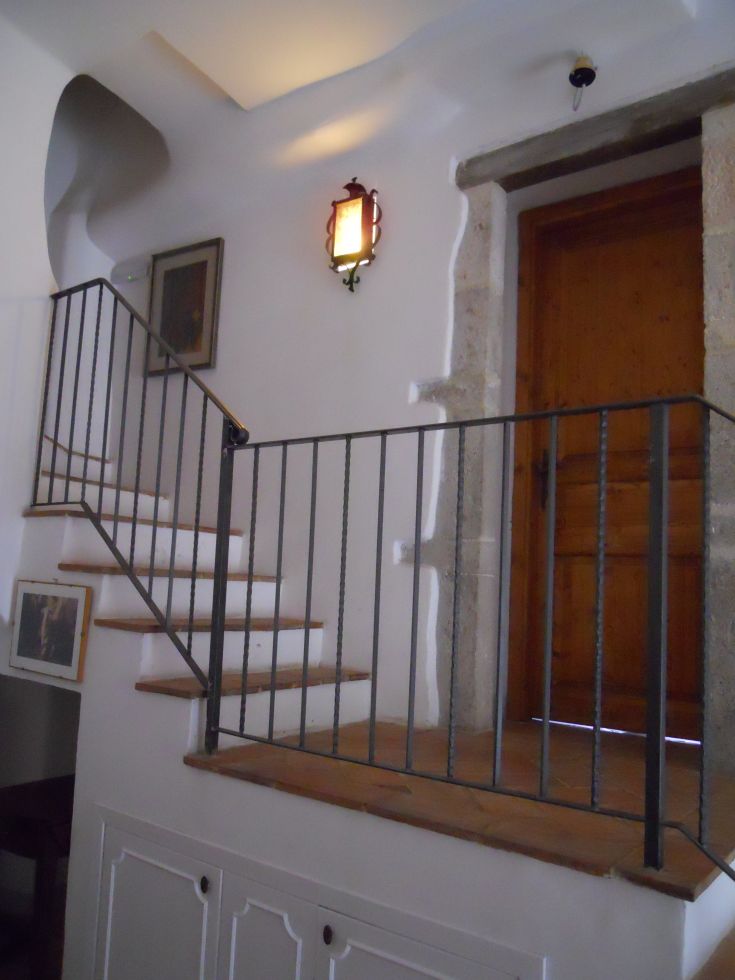 Interno di una guesthouse con scala in legno, luce calda che illumina l'ambiente e una porta in legno. Atmosfera rilassante e accogliente.