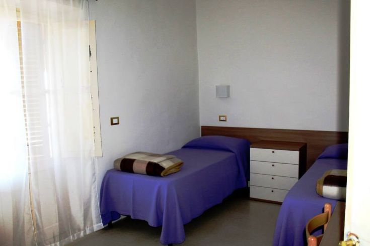 Camera semplice con letti singoli e tende leggere, ideale per un pernottamento sereno.