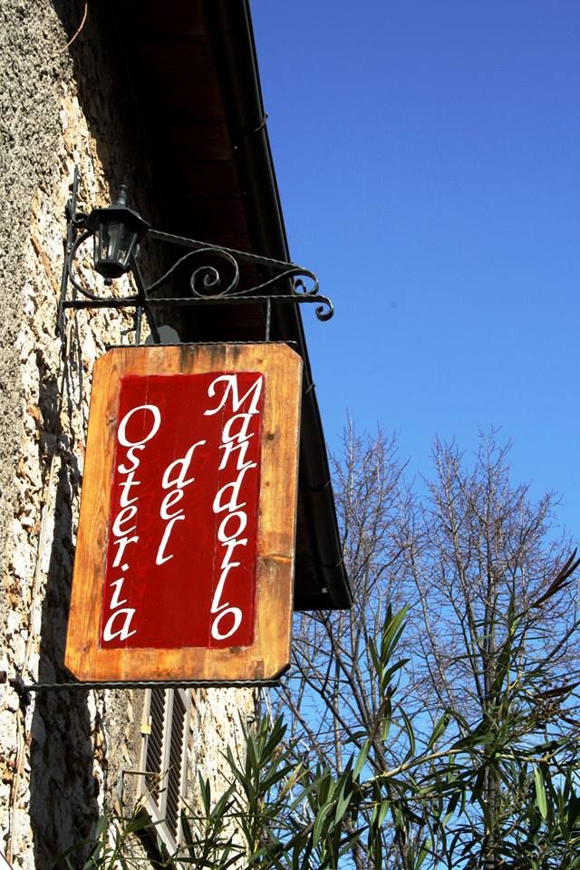 Insegna di un'osteria con sfondo blu e piante verdi circostanti.