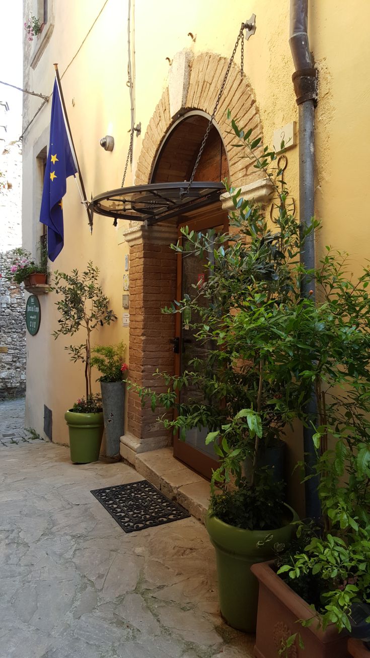 Simple entrance of Hotel Porta del Tempo in Stroncone, adorned with plants and decorations.