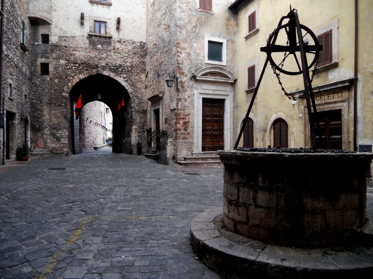 A medieval square featuring a well and historic arches.