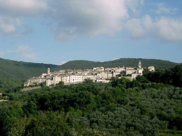 A panoramic view of a medieval village nestled among green hills.