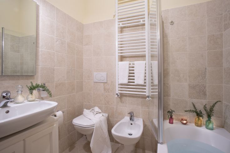 Bagno con piastrelle chiare, lavabo semplice e alcuni dettagli decorativi. Atmosfera tranquilla.