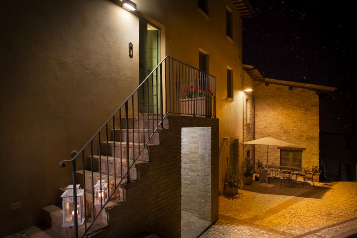 Scena notturna di un palazzo, con scalinate illuminate e lanterne, immerso in un ambiente decorato con piante.