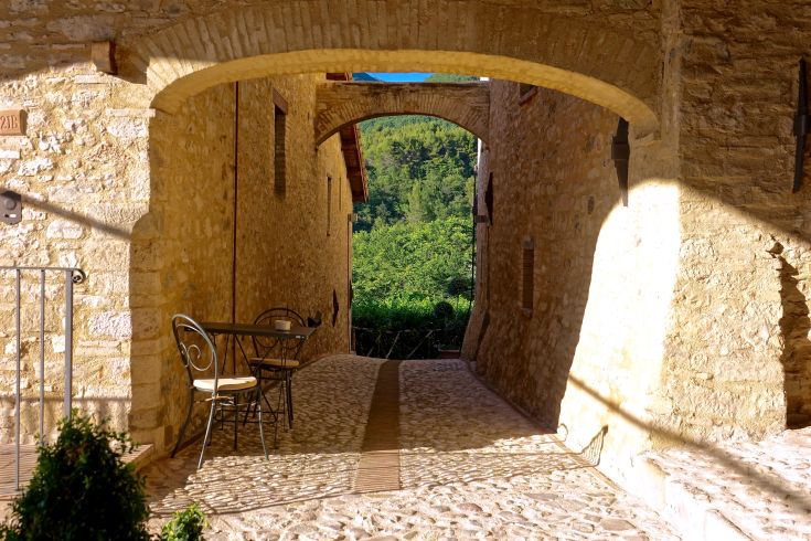 Un tranquillo vicolo di un vecchio borgo, con vista sulla natura circostante e una tavola apparecchiata per il relax.