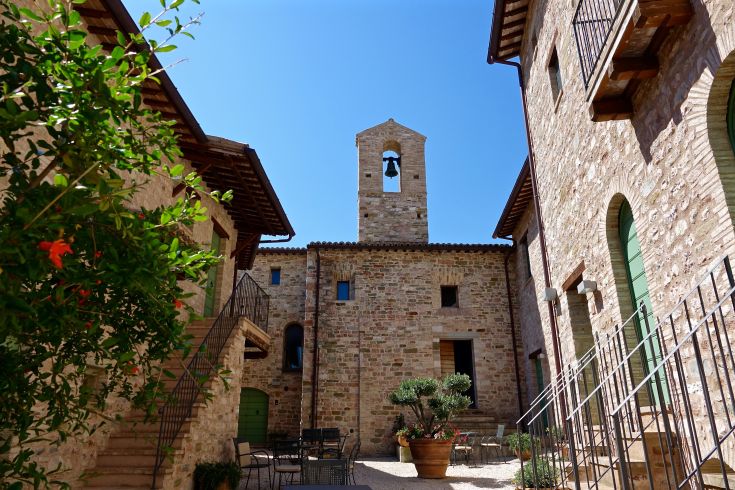 Un cortile caratterizzato da edifici in pietra e un campanile, situato in un ambiente tranquillo.