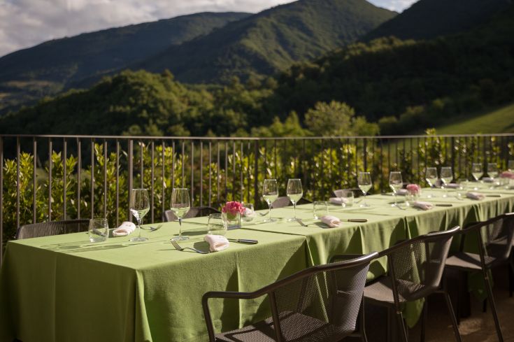 Tavolo all'aperto, circondato dalla natura umbra, preparato per accogliere gli ospiti.