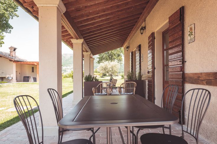 Area all'aperto di un agriturismo, attrezzata con tavolo e sedie, immersa nel verde.