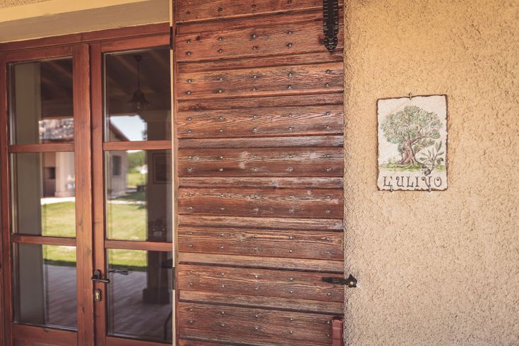 Dettaglio di una porta in legno con un'insegna decorativa che raffigura un ulivo.