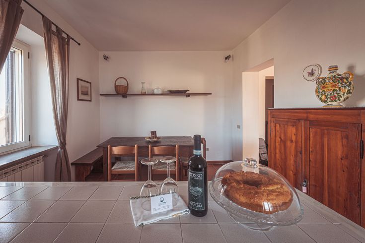 Interno semplice di un agriturismo, con tavolo in legno e una bottiglia di vino accanto a un dolce.