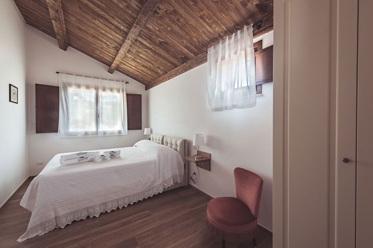 Camera confortevole di un agriturismo con arredi sobrii e soffitto in legno a vista.