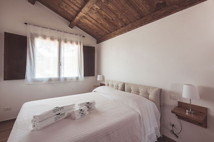 Camera semplice con un letto matrimoniale, una finestra che lascia entrare luce naturale e mobili in legno.