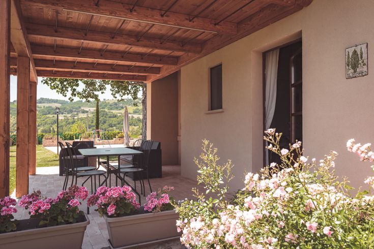 Accogliente area esterna di un agriturismo con panorama sulle colline. Fiori variopinti decorano il patio.