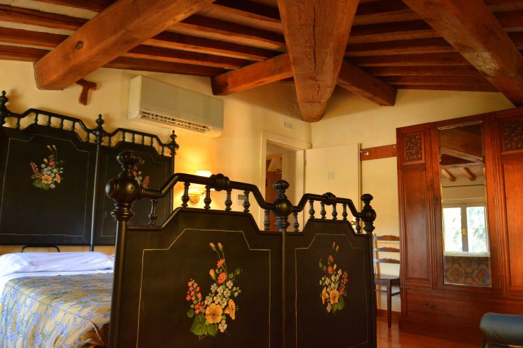 Camera semplice in una casa di campagna con travi in legno a vista e arredo sobrio.