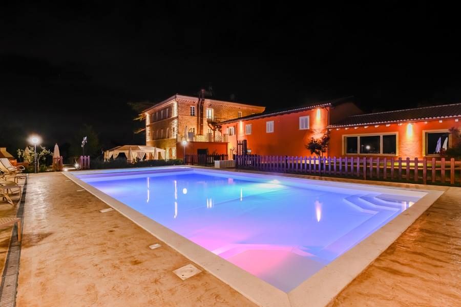 A pool surrounded by the lush Umbria landscape, beautifully lit in the evening, next to an elegant building.