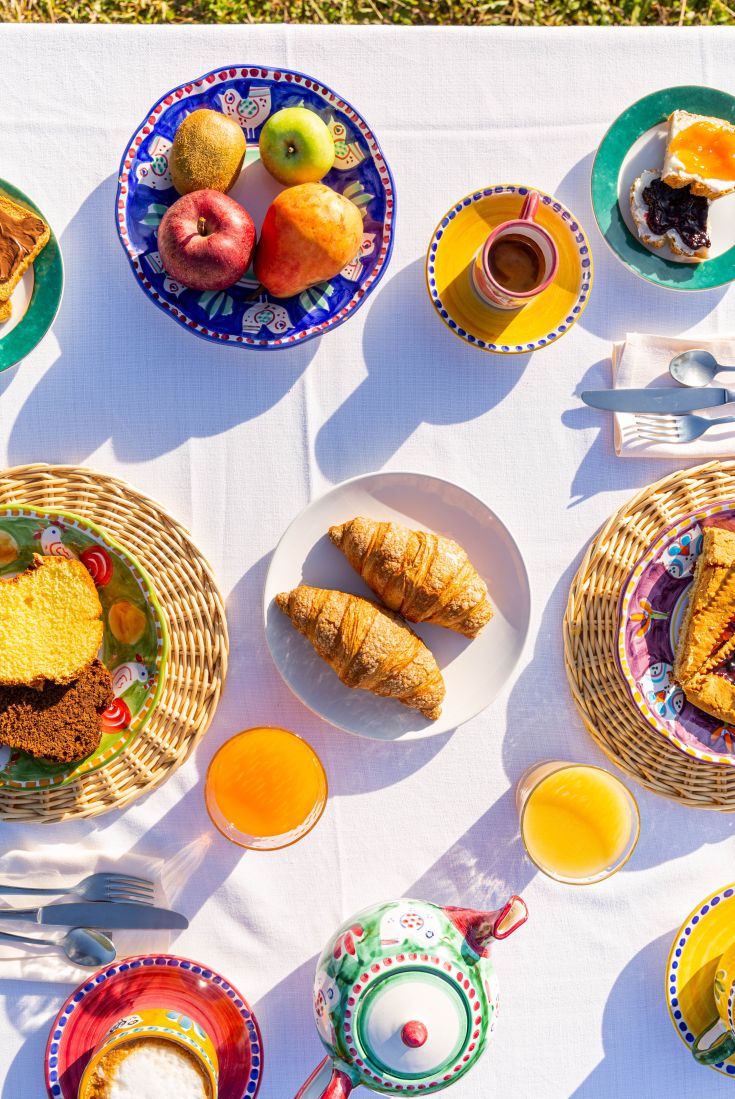 Colazione all'aperto con frutta, cornetti e bevande, immersi nella natura verde.