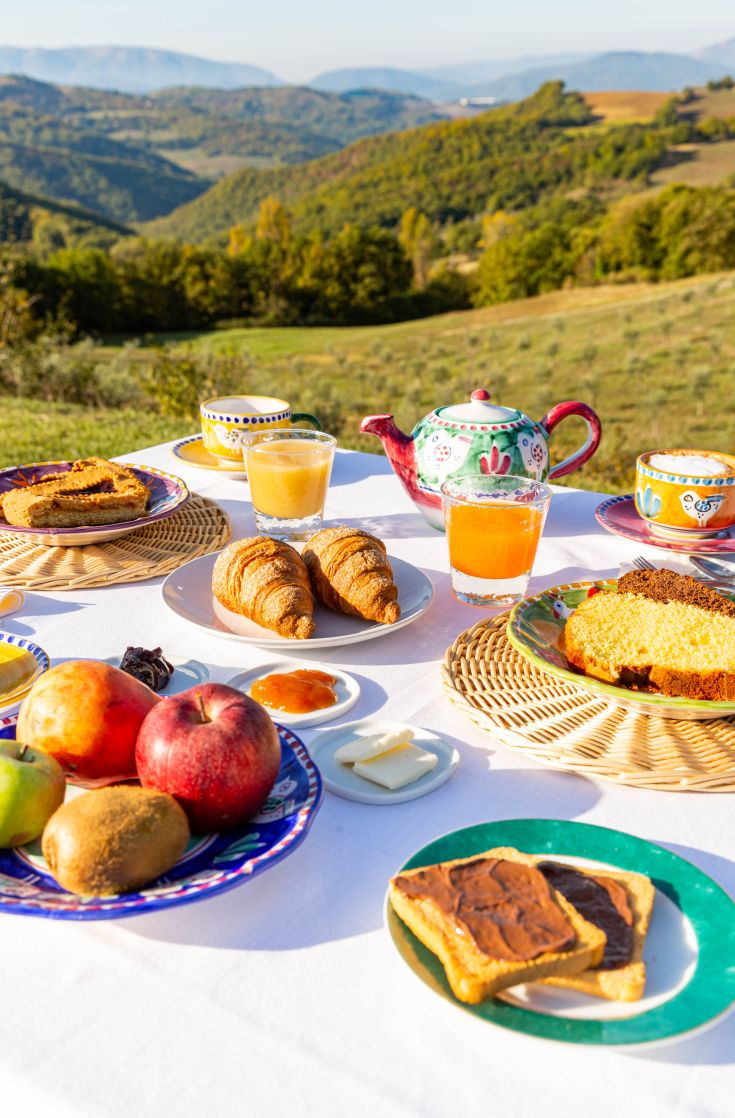Una colazione ricca su un tavolo all'aperto, circondato dalla natura tipica dell'Umbria.