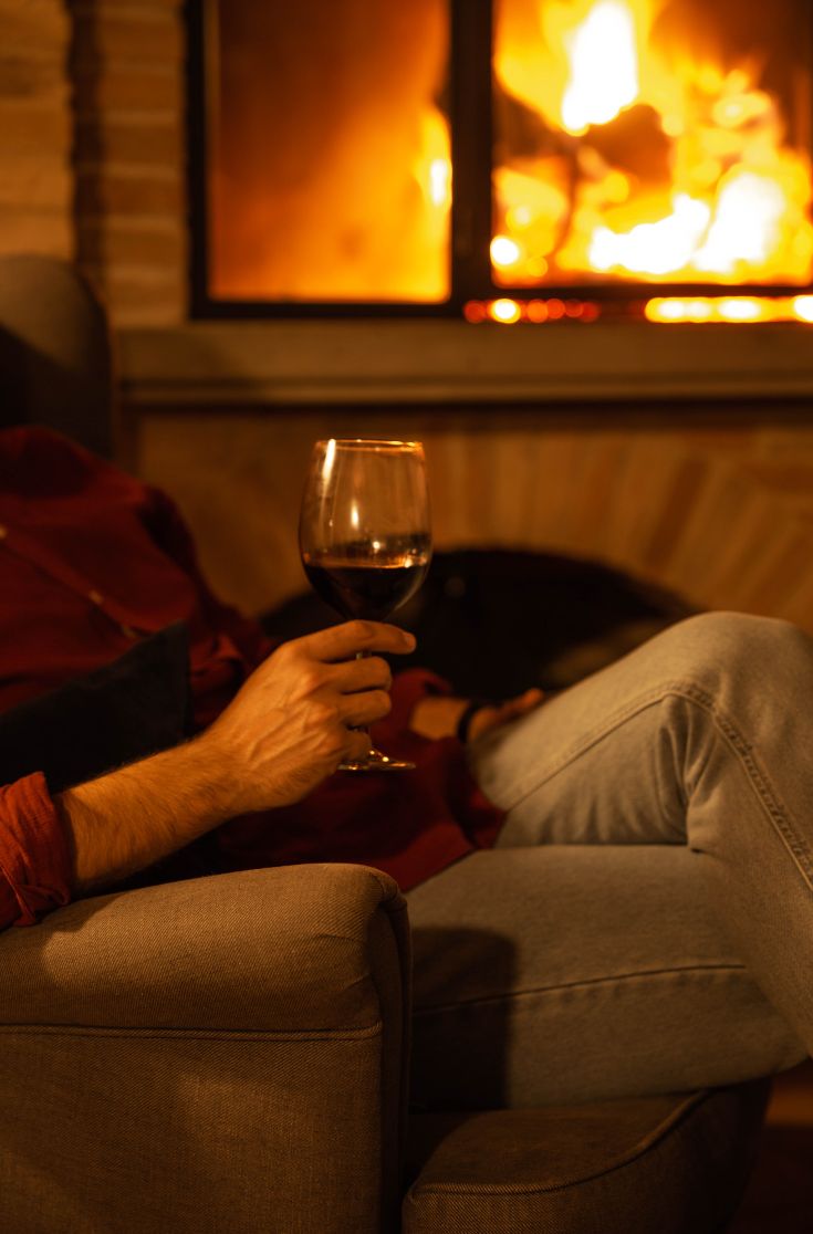 Un momento di relax accanto al camino con un bicchiere di vino rosso, in un ambiente caldo e accogliente.