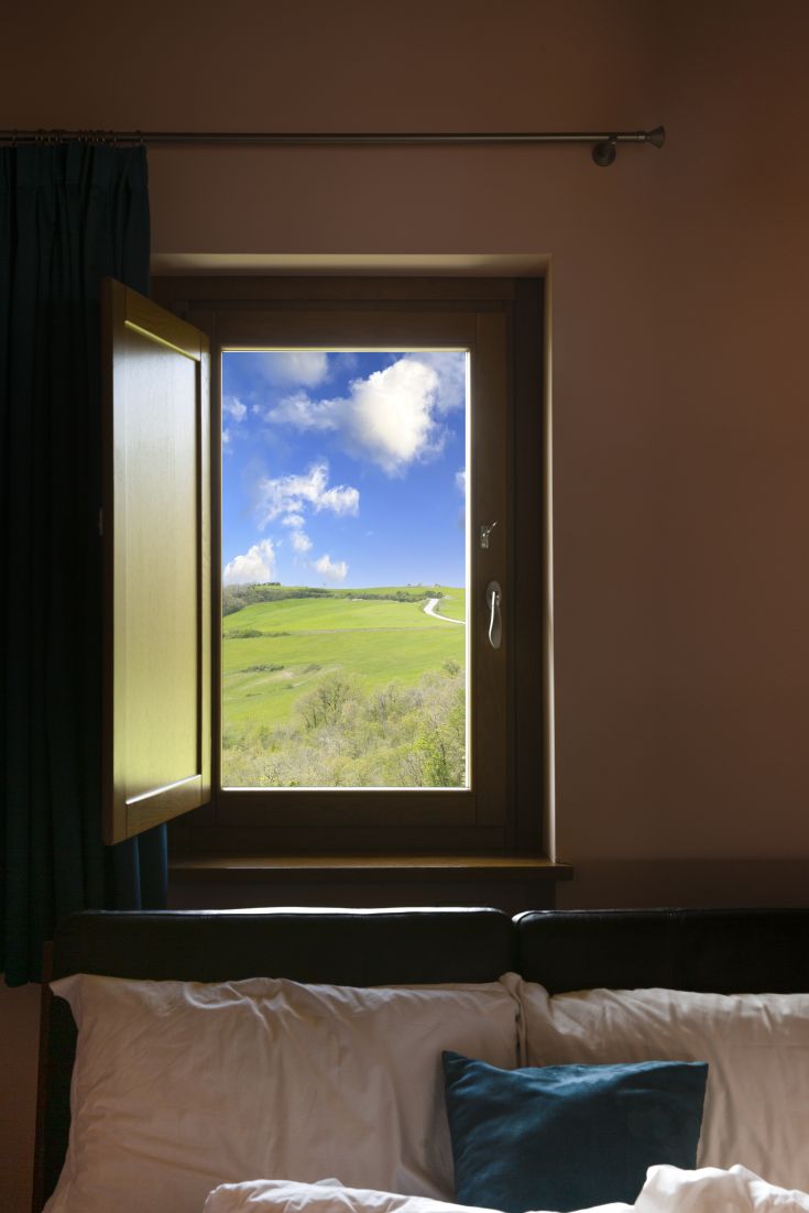 Scena di un paesaggio collinare verde visibile da una finestra, con alcune nuvole in un cielo sereno.