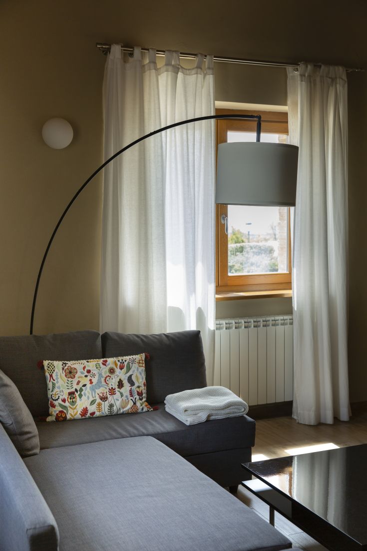 Un soggiorno sobrio con un divano grigio e luce naturale che entra dalle tende.