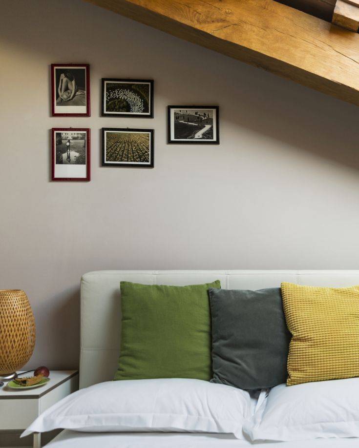 Camera semplice con cuscini di diverse tonalità e decorazioni appese alle pareti.