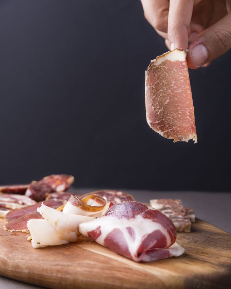 Varietà di salumi disposti su un tagliere in legno con sfondo semplice e neutro.