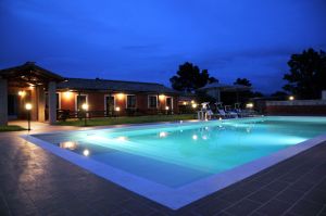 Piscina illuminata in un ambiente sereno, circondata da un edificio accogliente sotto il cielo stellato.