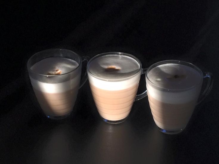 Tre tazze di bevande calde in un ambiente poco illuminato, con uno strato di schiuma bianca in cima.