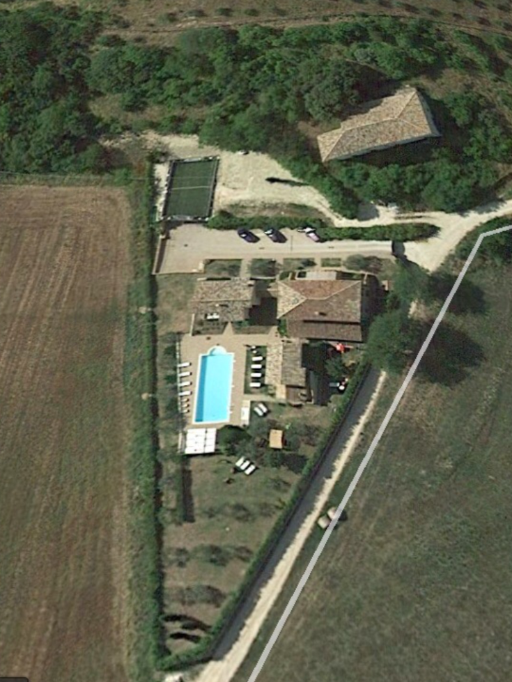 An aerial view of a building with a swimming pool, surrounded by the lush greenery of the Umbrian countryside.