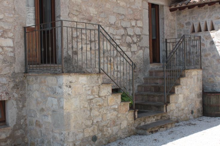 Stone staircase with a metal railing at a farmhouse surrounded by nature.