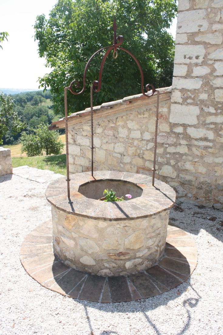 An old stone well with wrought iron elements, surrounded by lush vegetation.