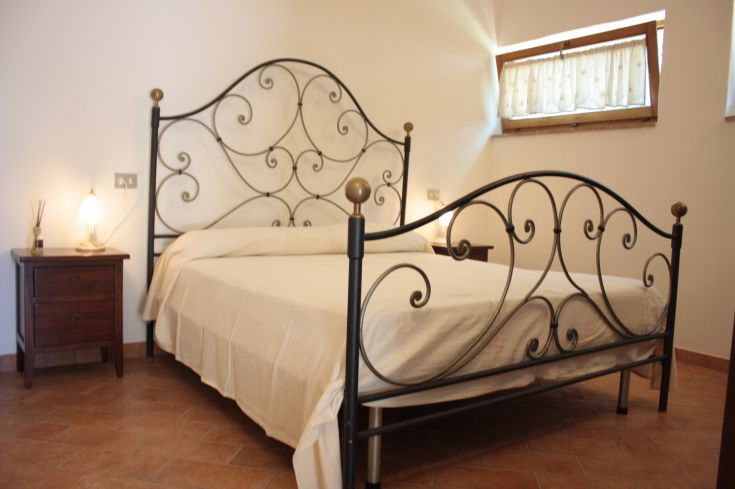 Quiet room with a wrought-iron bed and wooden details, located in an Umbrian agriturismo.