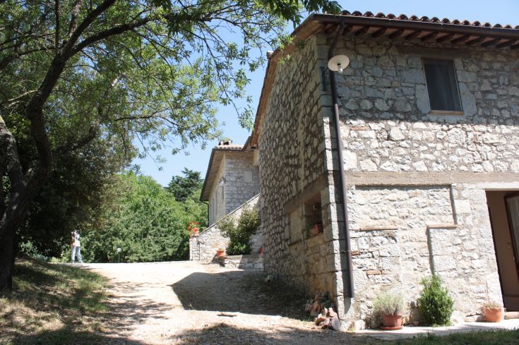 A farmhouse located in the Umbrian countryside, surrounded by vast green spaces and vegetation.