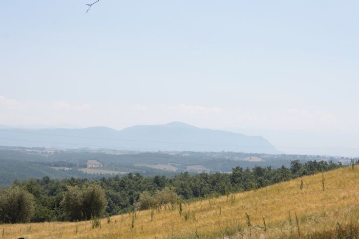 A hilly landscape of Umbria featuring green fields and distant mountain ridges.