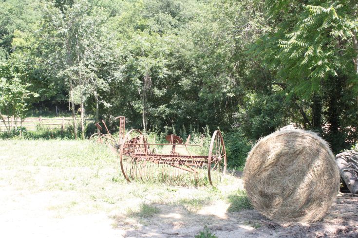 An antique farming equipment in a grassy field, with a hayroll in the foreground.