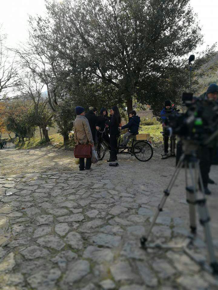A group of people gathers in a park, surrounded by trees and photography equipment.