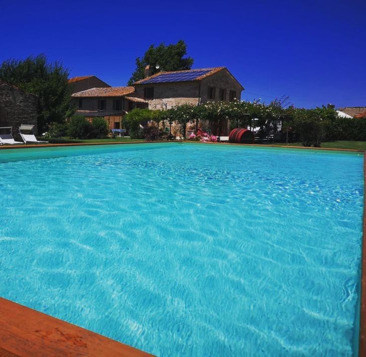 Une piscine naturelle bleue entourée par la nature, avec une maison rustique en arrière-plan.
