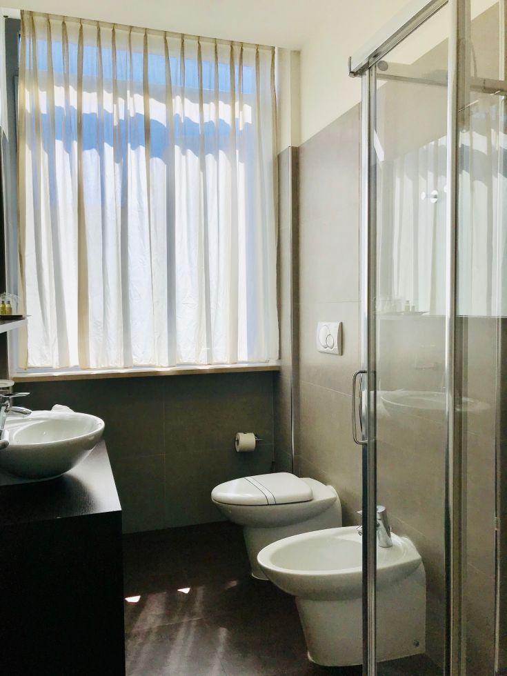 Une salle de bain lumineuse avec lumière naturelle et finitions simples; comprend une douche et un lavabo. Ambiance tranquille.