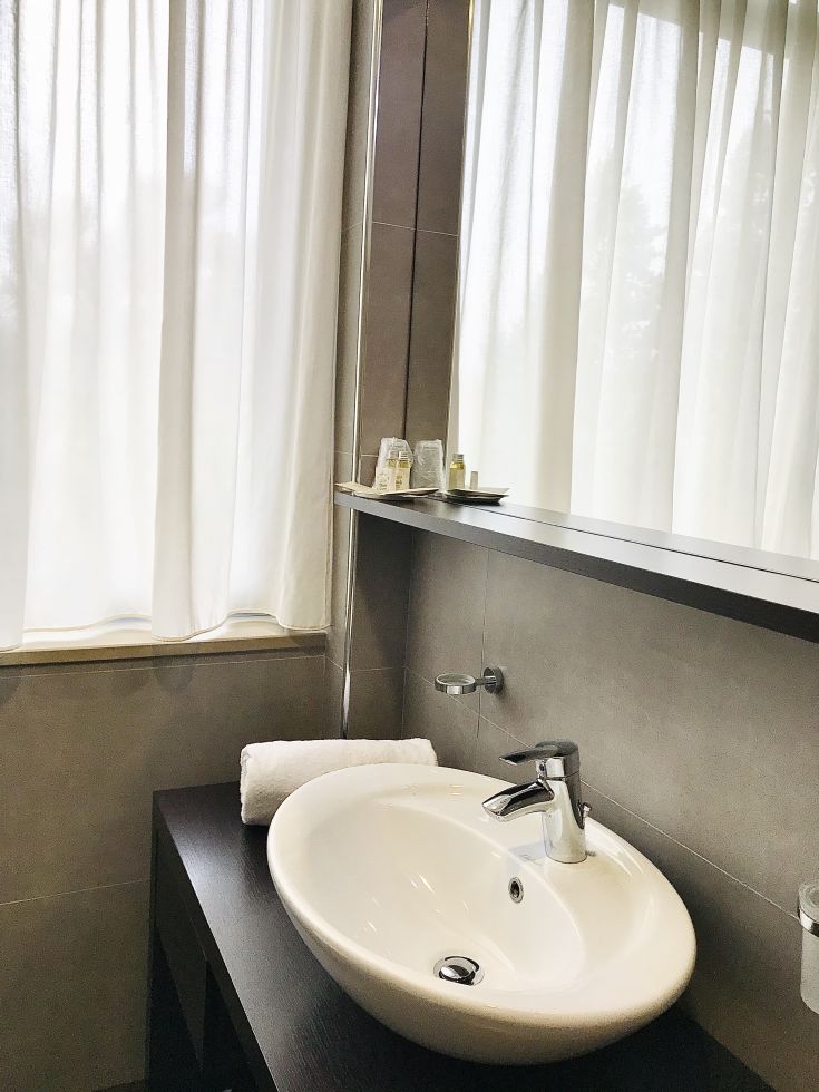 Une salle de bain contemporaine avec des équipements élégants, un lavabo et des rideaux clairs laissant entrer la lumière.