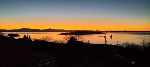 Tramonto sul Lago Trasimeno con tonalità di arancione e blu nel cielo sopra l'acqua.
