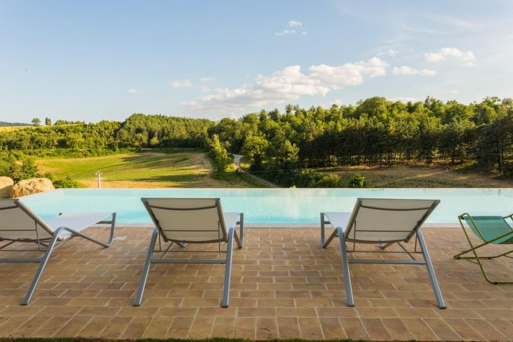 Scena della piscina con sdraio e paesaggio collinare intorno, un ambiente tranquillo e naturale.