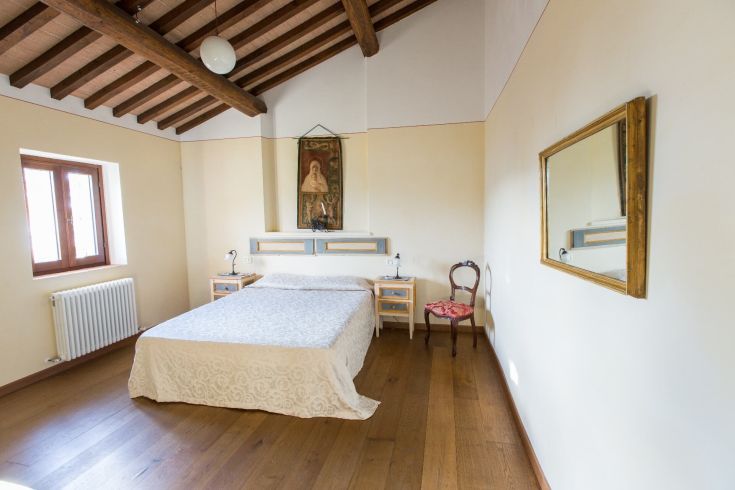 Camera ampia e luminosa con soffitto a travi in legno, letto matrimoniale e arredi in stile rustico. Spazio dedicato al relax.